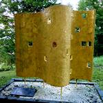 Kunstwerk: gelbe geschwungene Mauer mit kleinen Öffnungen