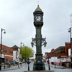 Alter gruener Turm mit Uhr inmitten eines kleinen Kreisverkehrs
